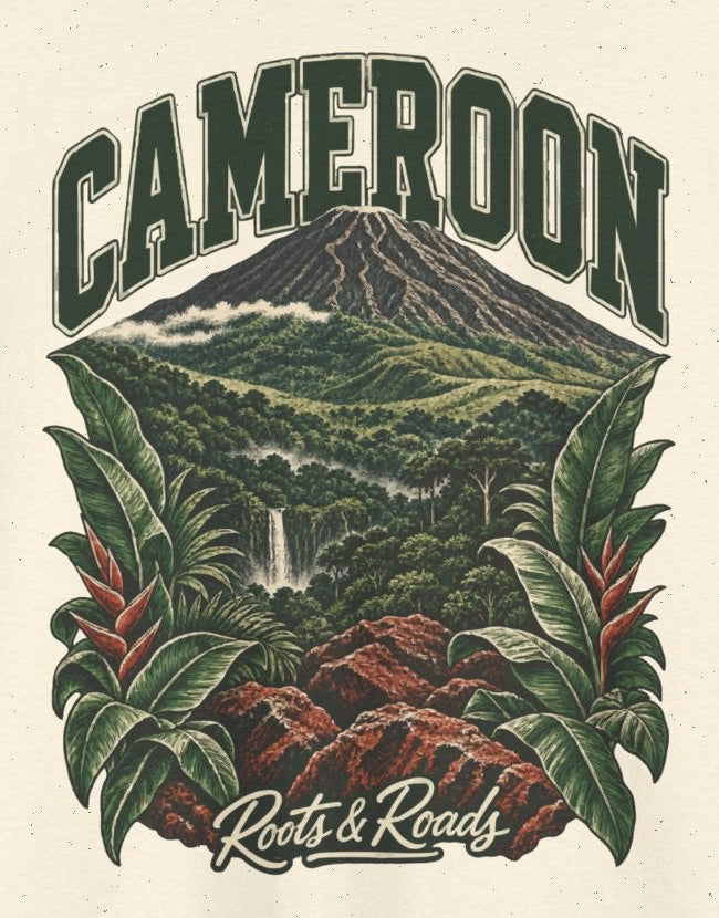 Print detail cropped from the Natural Cameroon supplier T-shirt mockup, showing green CAMEROON lettering above a forested volcano, waterfall, red rocks and broad tropical leaves and Roots & Roads script.