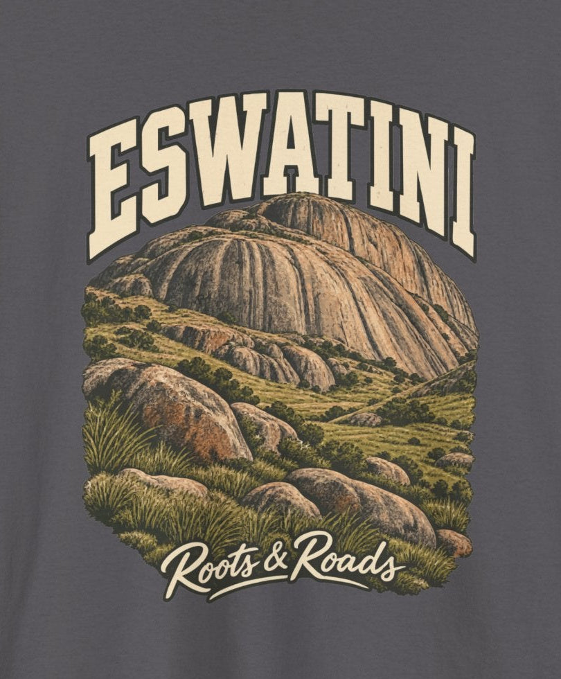 Print detail cropped from the Charcoal Eswatini supplier T-shirt mockup, showing cream ESWATINI lettering, rounded rock faces, grasses and boulders and Roots & Roads script.