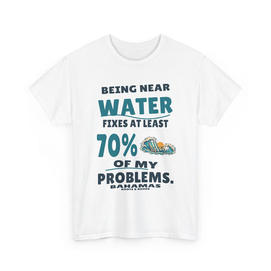 White Bahamas T-shirt, front view with “Being near water fixes at least 70% of my problems.” in oversized retro lettering, waves and a striped beach chair, Bahamas label and Roots & Roads signature.