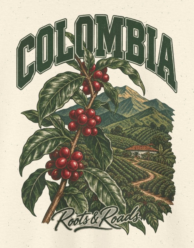 Print detail cropped from the Natural Colombia supplier T-shirt mockup, showing green COLOMBIA lettering above a coffee branch with red cherries and cultivated hills and Roots & Roads script.