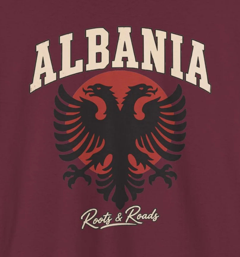 Close-up of the Albania Fresh Prints front design on Maroon cotton: cream arched lettering, a black double-headed eagle, muted red circle and Roots & Roads script. Cropped from the supplier mockup.