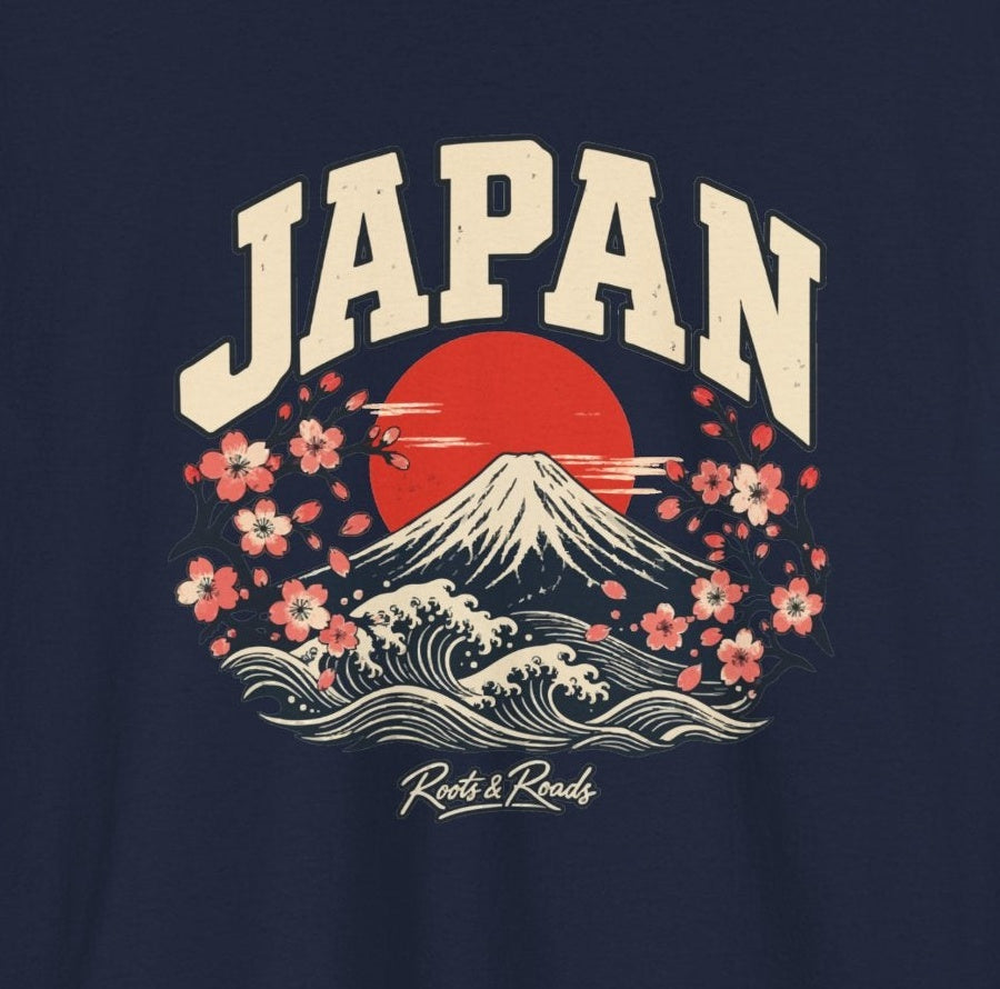 Close-up of the Japan Fresh Prints front design on navy cotton: cream arched lettering, Mount Fuji, a red sun, waves, cherry blossoms and Roots & Roads script.